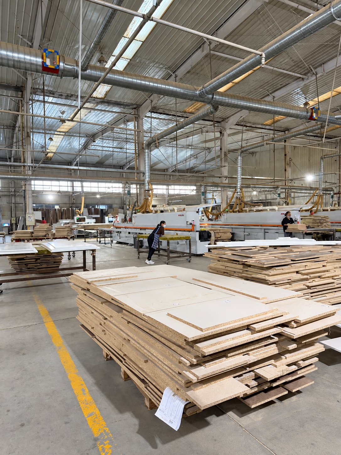 Production floor with stacked panel components and industrial processing equipment