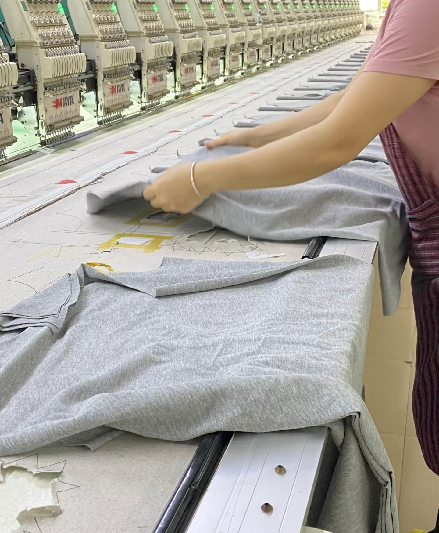 Worker handling garment pieces along an industrial embroidery production line